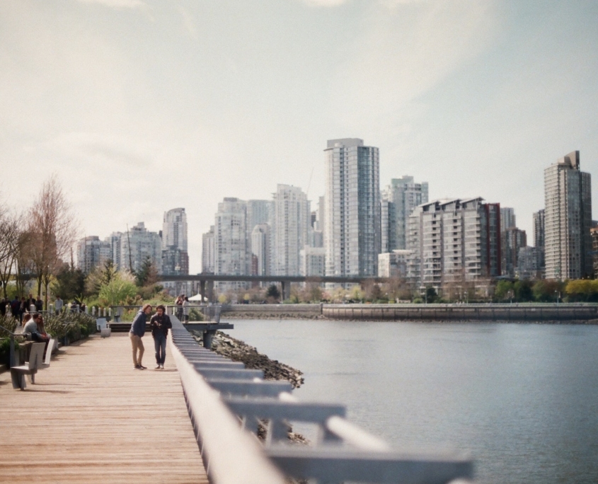 Two people walking along the Vancouver seawall with city buildings in the background. Reclaim Rehabilitation provides work services in a timely & effective manner